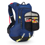 USWE Moto Hydro 12L hydration pack in navy blue with yellow waist buckles and reflective patches, front organizer pocket unzipped to show energy gels and nutrition bars stored in black mesh compartments with elastic retention straps, red hydration reservoir visible at top.