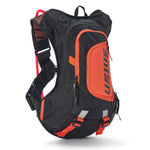 USWE Moto Hydro 12L hydration pack in black and orange colorway, side profile view showing elastic NDM 1.2 shoulder harness with mesh ventilation panels, red hydration hose routing, front zippered pocket with USWE logo, and orange bottom compression straps for securing gear during dirt bike rides.