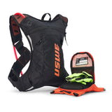 USWE Moto Hydro 3L hydration pack in black and orange with red hydration bladder visible through mesh side panel, displayed with detached front organizer pocket containing emergency card and neon yellow gloves alongside bright orange gear.