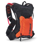 USWE Moto Hydro 3L hydration pack in black and orange colorway featuring bright orange detachable front organizer pocket with vertical USWE logo, mesh shoulder straps with orange and red accents, red hydration bladder visible through mesh side panel, and reflective gray trim details.