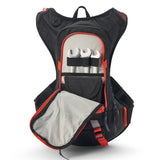USWE Moto Hydro 8L hydration pack in black with orange trim, main compartment fully unzipped to expose internal tool organizer holding three chrome wrenches secured by black elastic straps, gray padded interior lining, mesh storage pocket, and red waist belt buckle for dirt bike tool carrying.