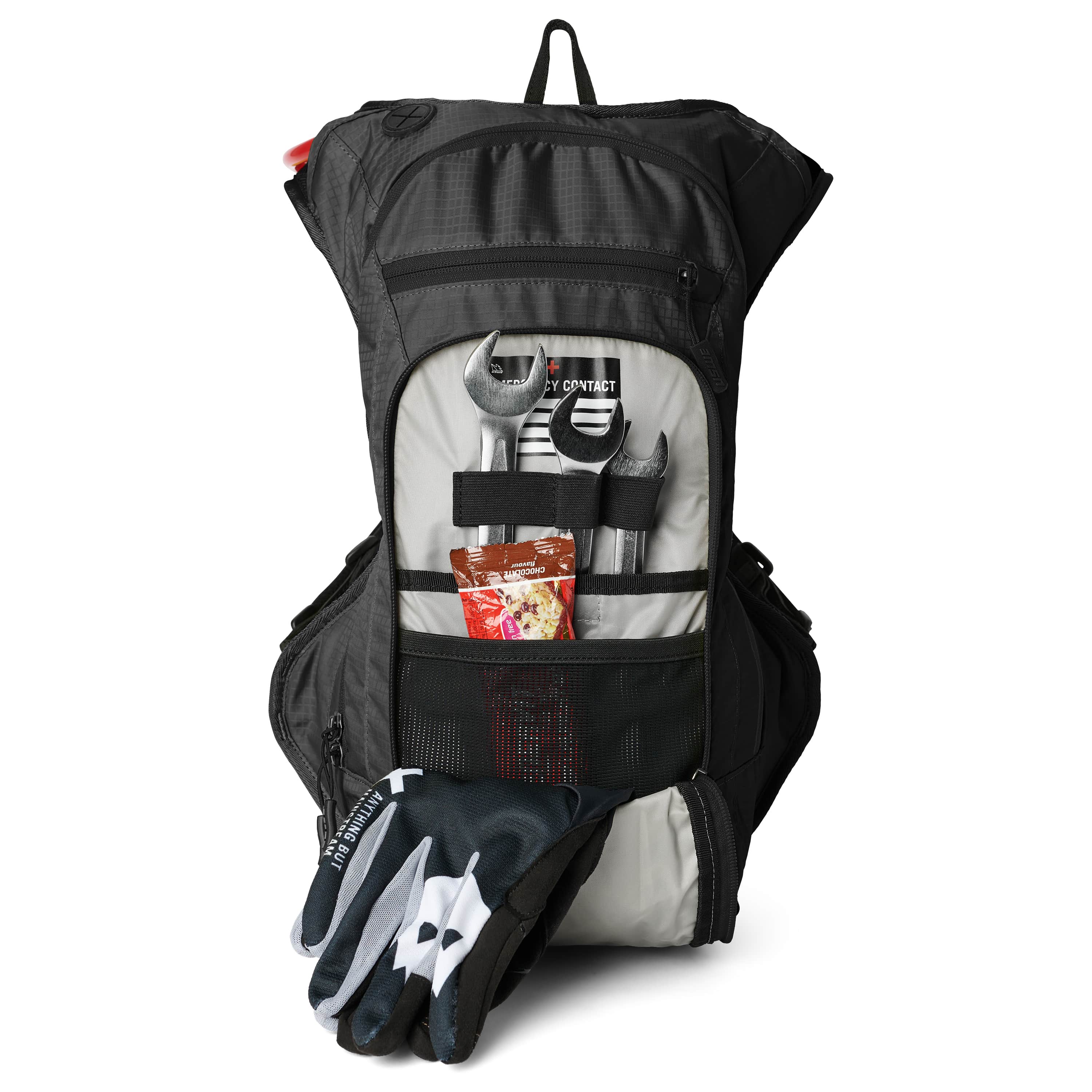 USWE OUTLANDER Moto 9L hydration pack in Black standing upright with front tool pocket fully opened showing wrenches, emergency contact card, energy bar, and motorcycle gloves secured with elastic retention straps against gray interior lining.