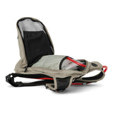 USWE OUTLANDER Moto 9L hydration pack in Sand with main compartment open showing 3L Elite bladder with red cap positioned inside, black mesh divider pocket, and red elastic NDM harness straps laid flat on white background.
