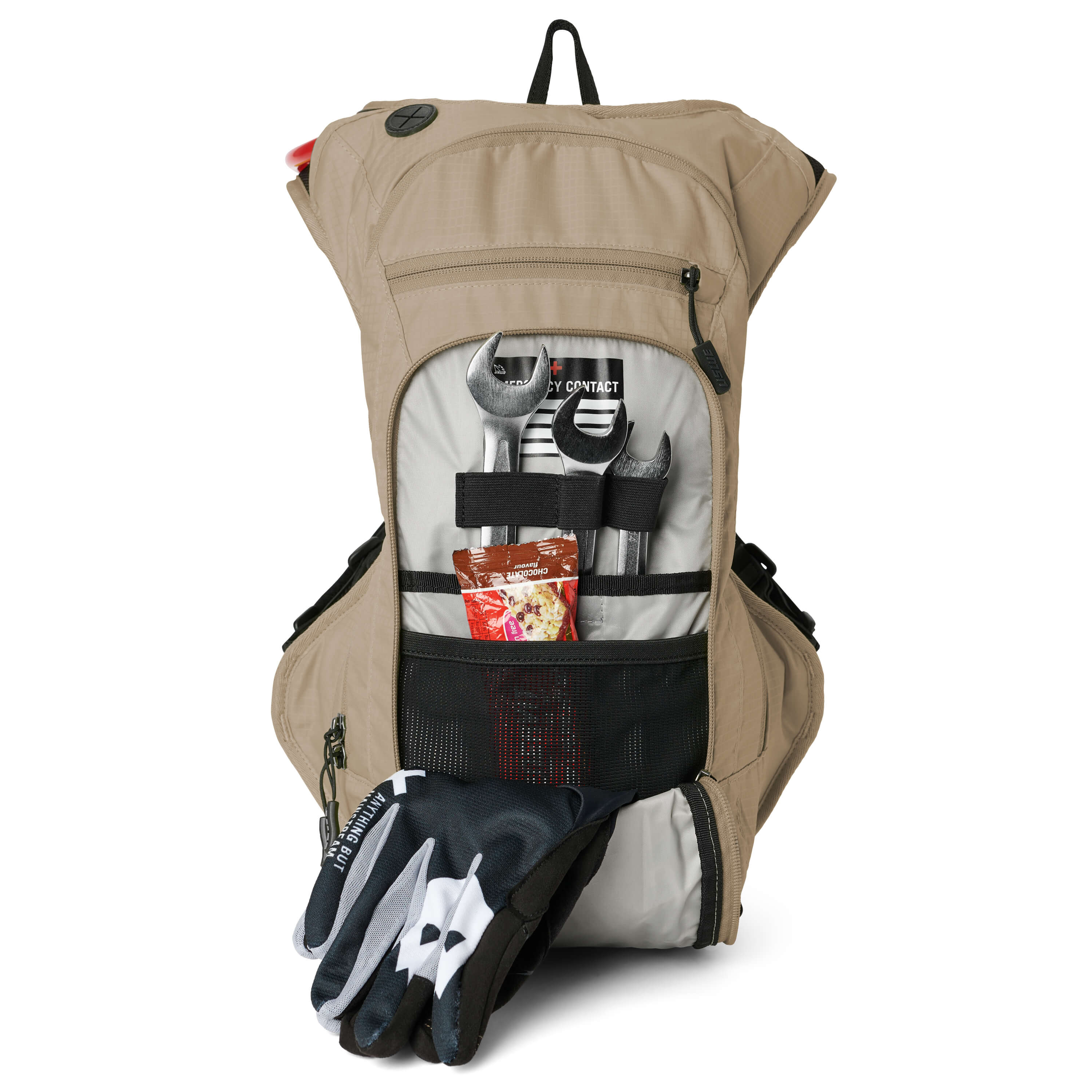 USWE OUTLANDER Moto 9L hydration pack in Sand colorway displayed vertically with front tool pocket unzipped exposing chrome wrenches, emergency contact card, and energy bar secured by black elastic straps, plus dirt bike gloves positioned at base of pack.